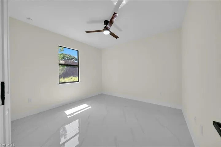 Spacious room featuring light-toned walls, contemporary ceiling fan, single window, and light grey tile flooring