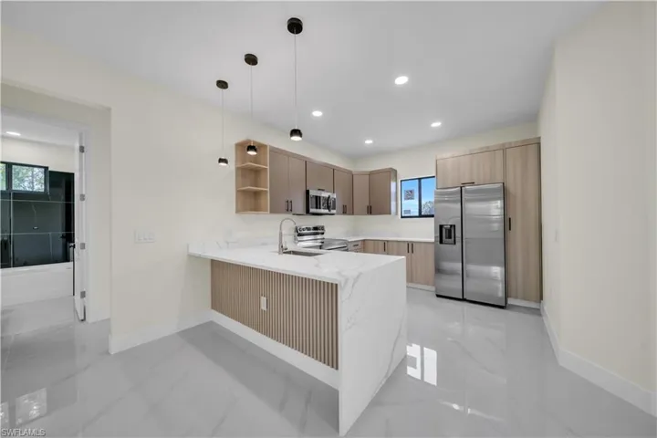 Contemporary kitchen with a waterfall island featuring a slatted wood-finish panel, white stone-finish countertops, and stainless steel appliances