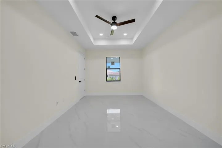 Spacious room featuring large format tile flooring, a tray ceiling with recessed lighting, and a modern ceiling fan