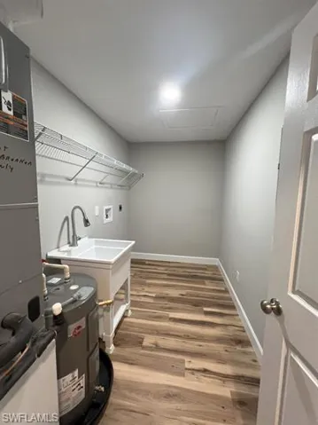 Laundry area with attic access, hookup for a washing machine, light wood-style flooring, electric water heater, and heating unit