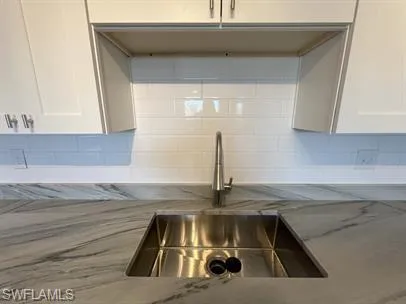 Kitchen with decorative backsplash, white cabinets, and light stone countertops