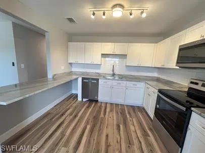 Kitchen featuring appliances with stainless steel finishes, white cabinetry, dark wood finished floors, and light countertops
