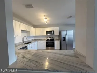 Kitchen with stainless steel appliances, white cabinets, and light stone counters