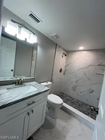 Bathroom featuring a marble finish shower, light marble finish flooring, and vanity