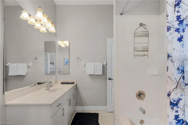 Full bathroom with vanity, shower / bathtub combination with curtain, tile patterned floors, and a chandelier
