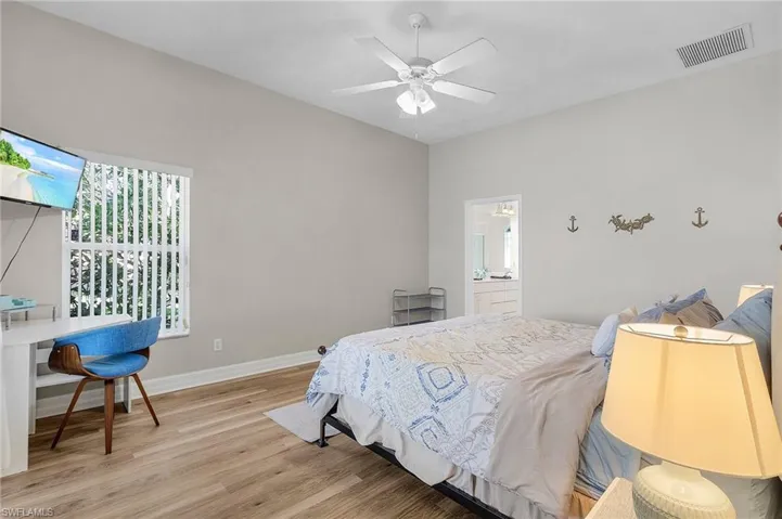 Bedroom with light wood-style floors, multiple windows, ensuite bathroom, and ceiling fan