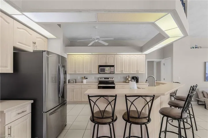 Kitchen with stainless steel appliances, a ceiling fan, light tile patterned flooring, a kitchen bar, and light countertops