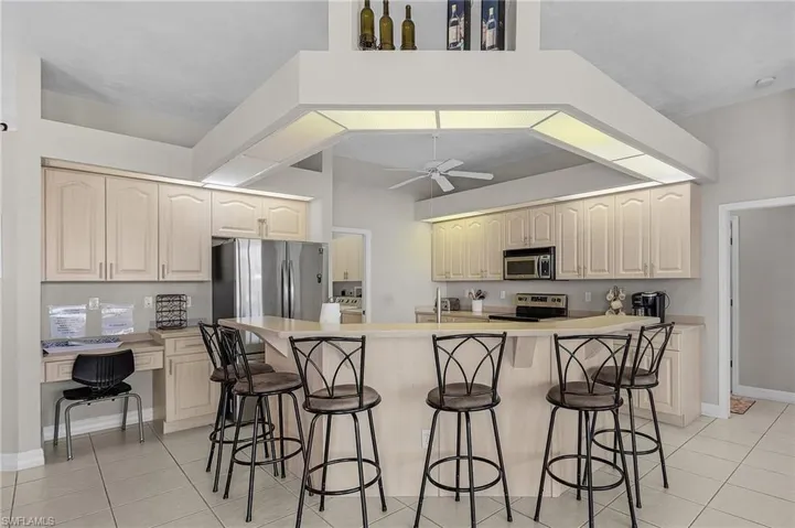 Kitchen with a breakfast bar area, appliances with stainless steel finishes, light tile patterned flooring, and built in study area