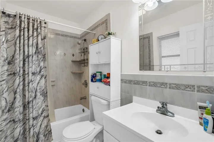 Full bathroom featuring tile walls, shower / bathtub combination with curtain, toilet, and vanity