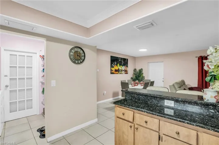 Kitchen featuring light brown cabinetry, dark stone countertops, ornamental molding, and light tile patterned floors