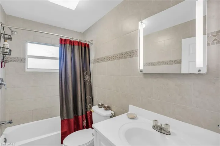 Full bathroom featuring tile walls, toilet, vanity, and shower / tub combo with curtain