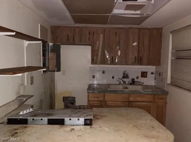 Kitchen with open shelves, brown cabinetry, and light stone countertops
