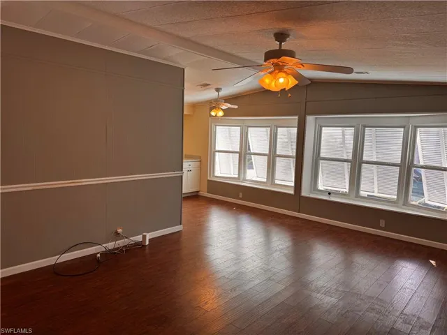 Spare room with lofted ceiling, dark wood-type flooring, baseboards, visible vents, and ceiling fan