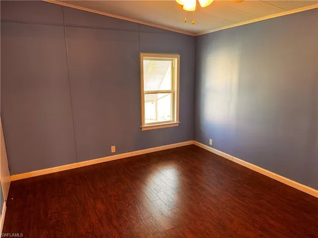 Empty room featuring baseboards, crown molding, dark wood-type flooring, and a ceiling fan