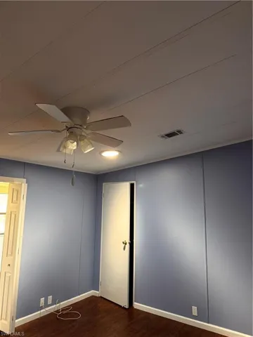 Empty room with baseboards, visible vents, ceiling fan, and dark wood-type flooring