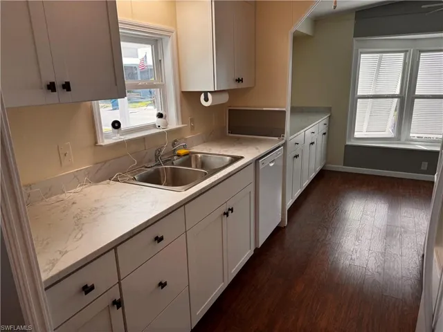 Kitchen featuring light countertops, a sink, dishwasher, white cabinets, and dark wood-type flooring