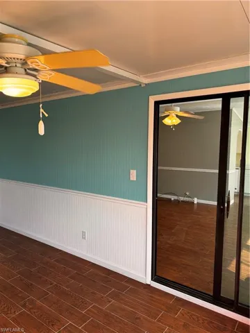 Empty room with a wainscoted wall, crown molding, wood finished floors, and a ceiling fan