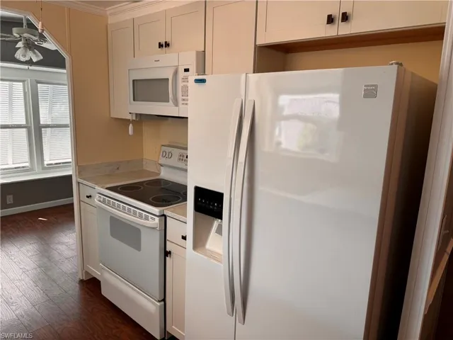Kitchen with light countertops, white appliances, baseboards, a ceiling fan, and dark wood finished floors