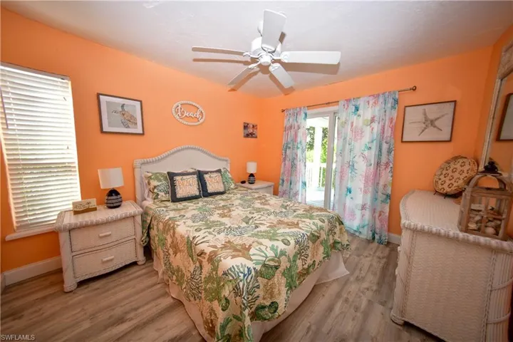 Bedroom featuring a ceiling fan, wood-finish flooring, a window with blinds, and white patio doors