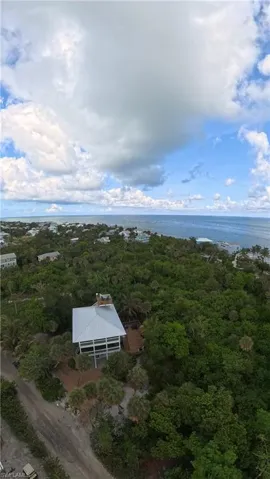 Coastal property featuring a metal roof, multiple balconies, a surrounding dense tree canopy, and direct proximity to the ocean