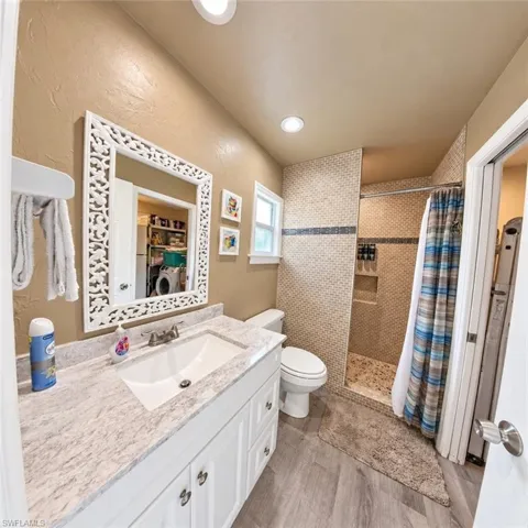 Bathroom featuring white cabinetry, stone-finish vanity countertop, recessed lighting, walk-in shower with tiled surround, and wood-finish flooring