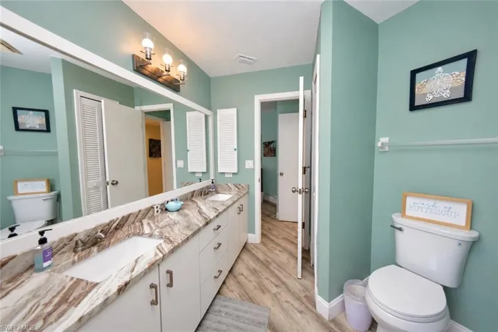 Extended vanity featuring stone-finish countertop, dual-basin integrated sink, wood-finish flooring, and wall-mounted three-light fixture