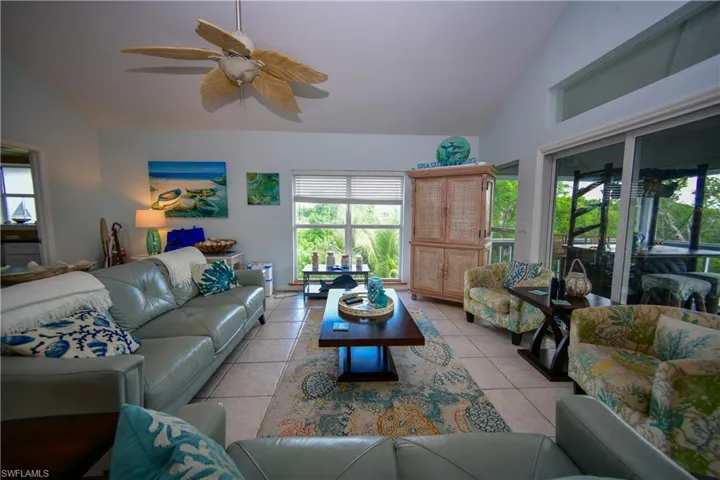 Bright living area featuring vaulted ceilings, tile flooring, a tropical-style ceiling fan, large windows, and sliding glass doors opening to an outdoor area
