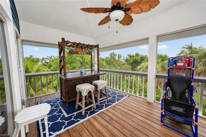 Screened-in porch featuring wood-plank decking, white railings, and a ceiling-mounted palm-leaf style paddle fan