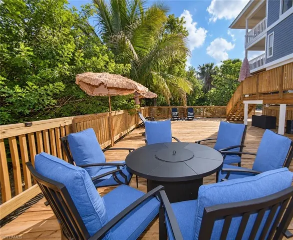 Spacious wood deck featuring wood railings, exterior staircase, and mature tropical landscaping