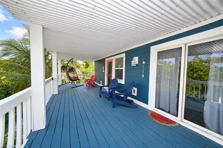 Covered outdoor deck featuring painted wood-plank flooring, white railing, corrugated ceiling, and sliding glass door access