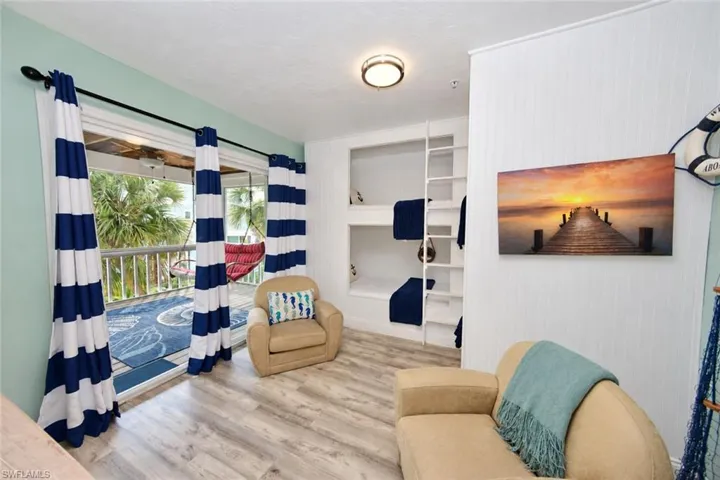 Built-in bunk beds with integrated ladder, wood-finish flooring, beadboard wall paneling, and access to an exterior deck via sliding glass doors