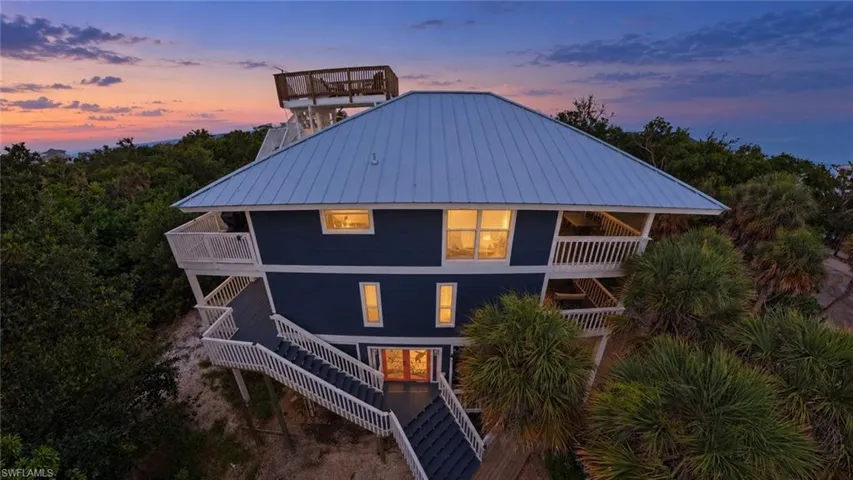 Multi-level residence featuring a metal roof, rooftop observation deck, wrap-around balconies with white railings, and lap siding