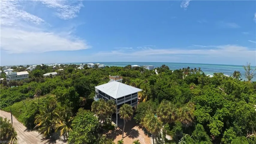 Elevated structure with a metal roof, expansive wraparound balconies, and abundant mature palm trees
