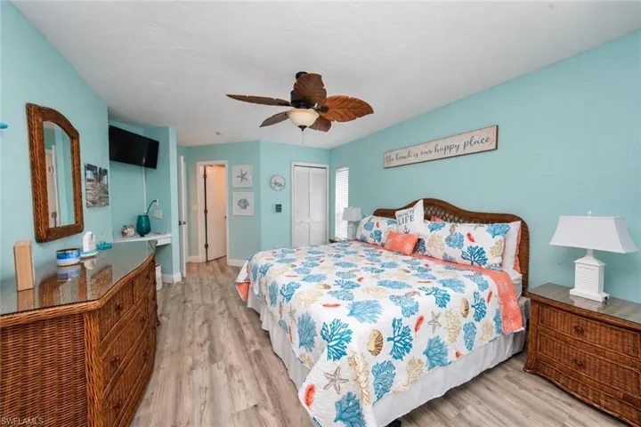 Room featuring wood-finish flooring, a ceiling fan with leaf-shaped blades, and louvered closet doors