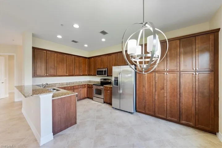 Kitchen featuring kitchen peninsula, sink, light stone countertops, hanging light fixtures, and appliances with stainless steel finishes