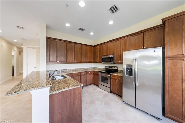 Kitchen with light tile patterned floors, appliances with stainless steel finishes, kitchen peninsula, sink, and light stone counters