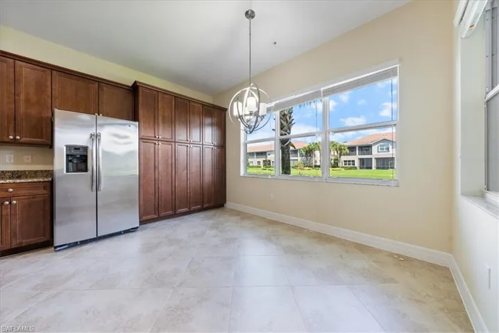 Kitchen with decorative light fixtures, light stone counters, a notable chandelier, stainless steel refrigerator with ice dispenser, and dark brown cabinetry