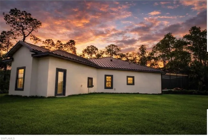 Back of property at dusk with stucco siding, a yard, and a standing seam roof