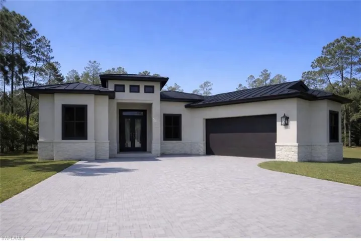 Prairie-style home featuring stone siding, a standing seam roof, an attached garage, decorative driveway, and a front lawn