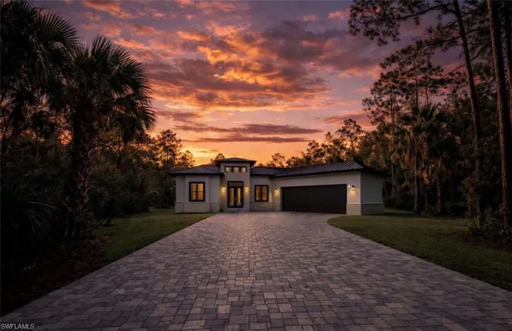 View of front of home with a yard, a garage, decorative driveway, stucco siding, and a metal roof