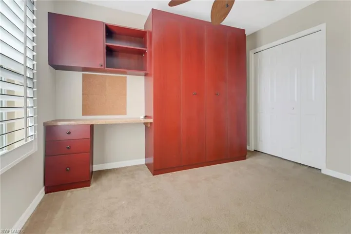 Unfurnished bedroom with light colored carpet, a ceiling fan, baseboards, a closet, and built in desk