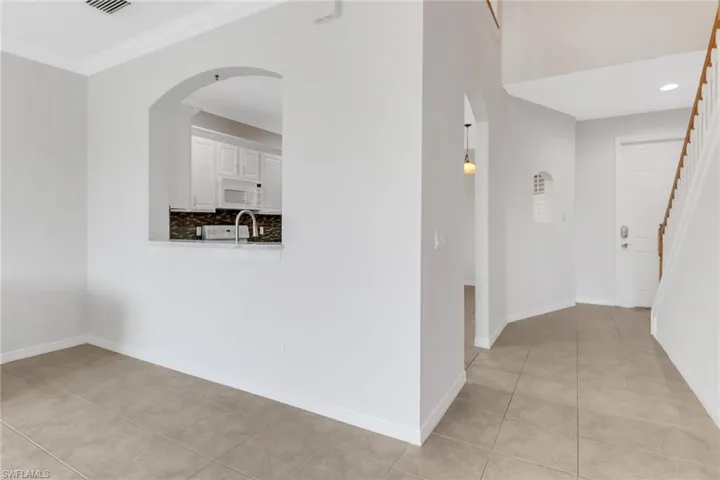 Hall with arched walkways, light tile patterned flooring, baseboards, stairs, and crown molding