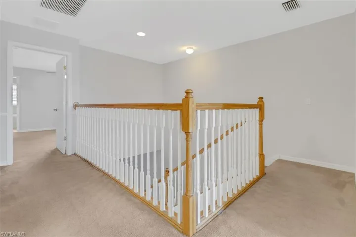 Hallway with carpet floors, an upstairs landing, and visible vents