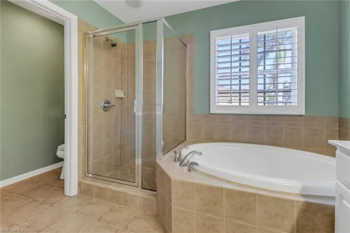 Bathroom featuring a garden tub, toilet, a stall shower, tile patterned flooring, and baseboards