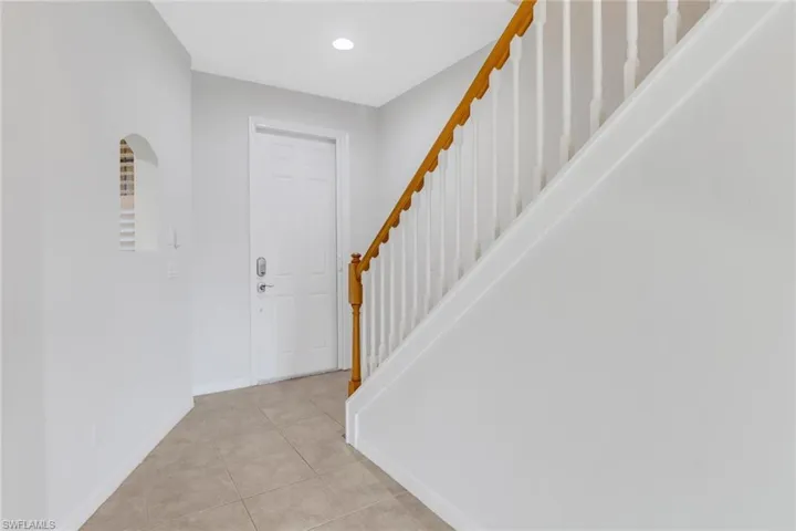 Foyer entrance featuring light tile patterned floors, baseboards, arched walkways, stairway, and recessed lighting