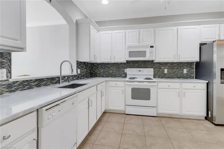 Kitchen with tasteful backsplash, white appliances, a sink, and white cabinets