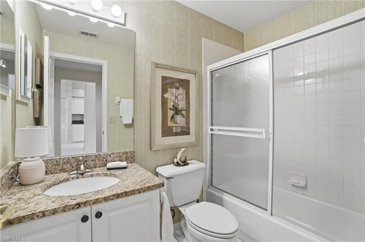 Full bath with wallpapered walls, vanity, and enclosed tub / shower combo
