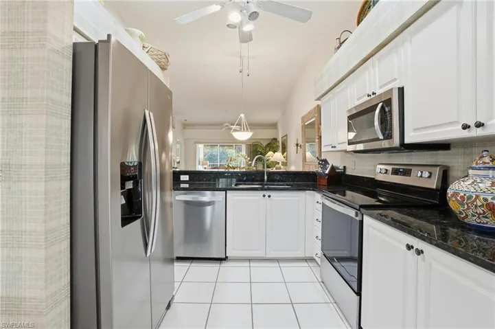 Kitchen featuring stainless steel appliances, dark stone counters, white cabinets, light tile patterned flooring, and lofted ceiling