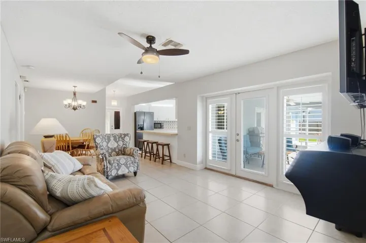 Open-concept living area featuring light tile flooring, a ceiling fan, and white French doors with louvered inserts providing access to the exterior