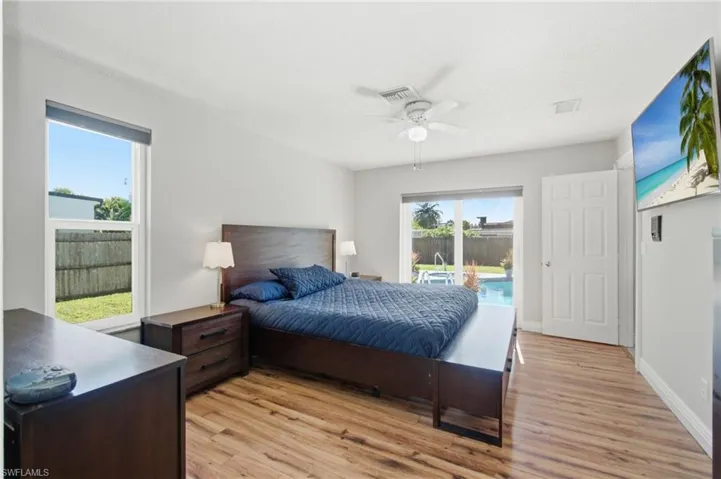 Spacious master bedroom featuring wood-finish flooring, a ceiling fan, and direct access to a private backyard with a swimming pool